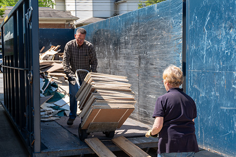 Man and Woman Walking Debris Into Large Dumpster